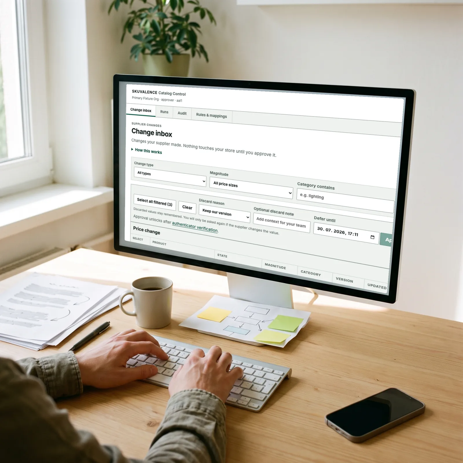 Over-the-shoulder view of a sunny desk with Skuvalence Catalog Control open, showing supplier catalogue changes awaiting review, beside notes and coffee
